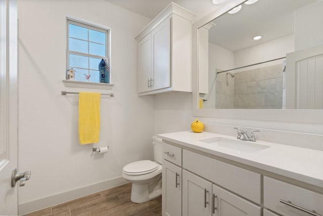 full bath featuring toilet, wood finished floors, tiled shower, baseboards, and vanity