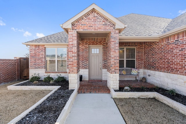 doorway to property featuring brick siding, a shingled roof, and fence