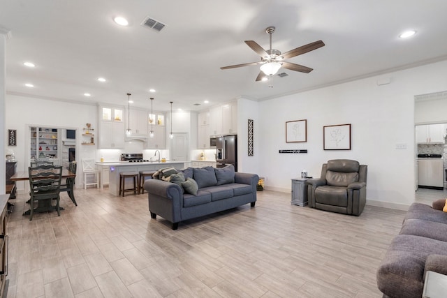 living room featuring sink, ornamental molding, light hardwood / wood-style floors, and ceiling fan