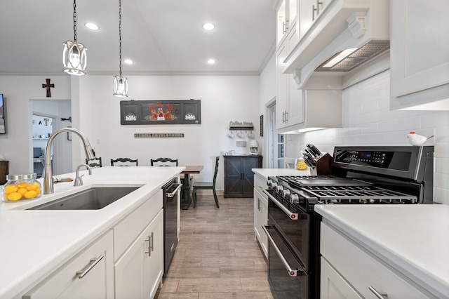 kitchen featuring tasteful backsplash, under cabinet range hood, double oven range, white cabinets, and a sink