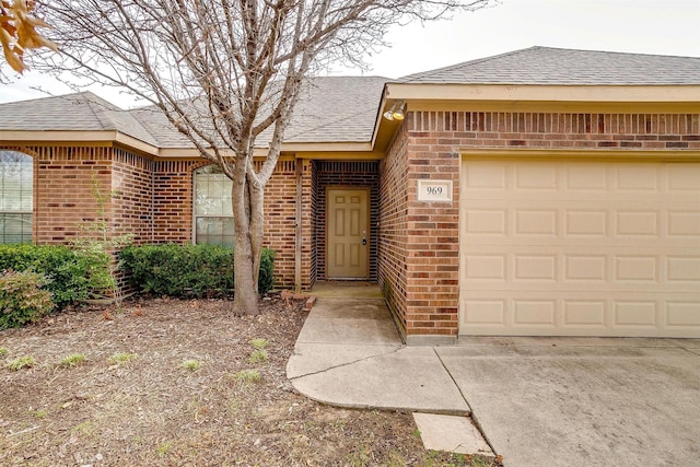 doorway to property with a garage, brick siding, and roof with shingles