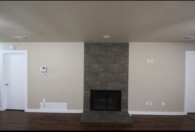 unfurnished living room featuring dark hardwood / wood-style flooring, a tiled fireplace, and a textured ceiling