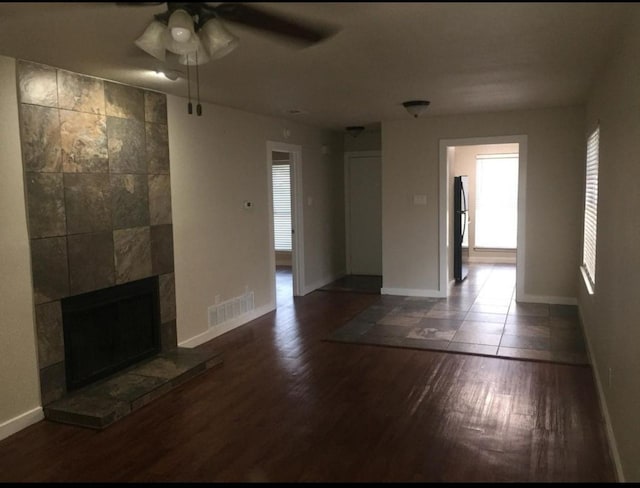 unfurnished living room featuring a tiled fireplace, dark hardwood / wood-style floors, and ceiling fan