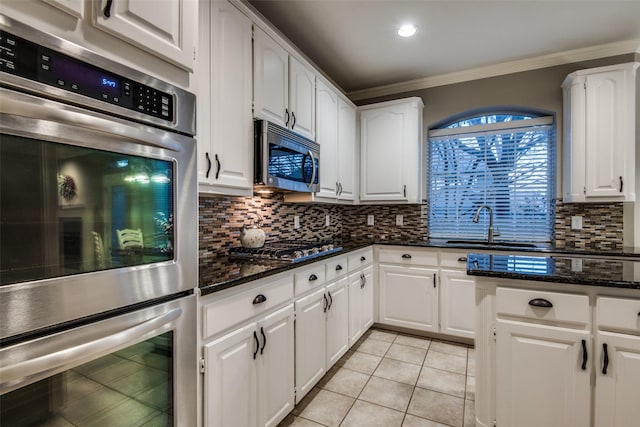 kitchen featuring white cabinetry, crown molding, stainless steel appliances, and dark stone countertops