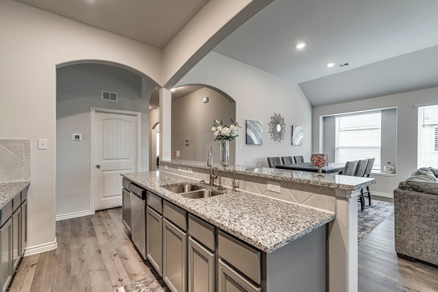 kitchen with stainless steel dishwasher, a kitchen island with sink, sink, and light wood-type flooring