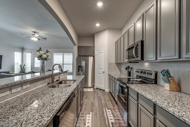 kitchen with light stone counters, stainless steel appliances, sink, and light hardwood / wood-style flooring