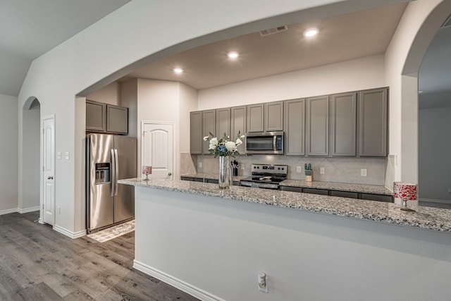 kitchen with gray cabinets, light stone countertops, appliances with stainless steel finishes, and decorative backsplash