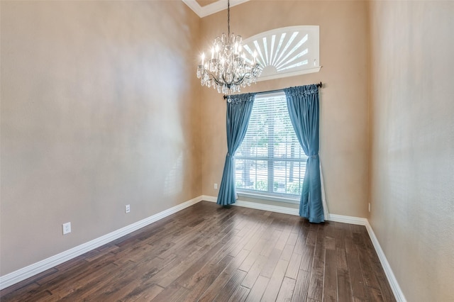 empty room with wood-type flooring, a towering ceiling, and a chandelier