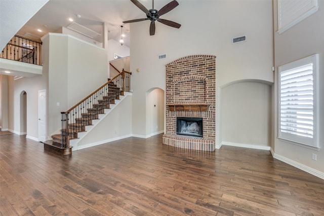 unfurnished living room featuring ceiling fan, a fireplace, dark hardwood / wood-style floors, and a towering ceiling