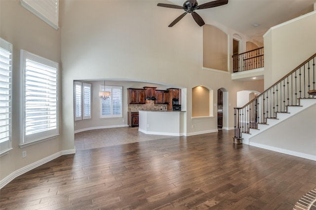 unfurnished living room featuring dark wood-type flooring, ceiling fan with notable chandelier, and a towering ceiling