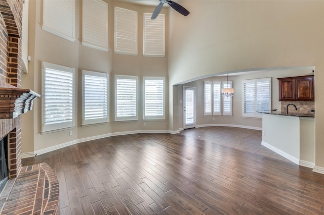 unfurnished living room featuring dark hardwood / wood-style floors, plenty of natural light, a fireplace, and ceiling fan with notable chandelier