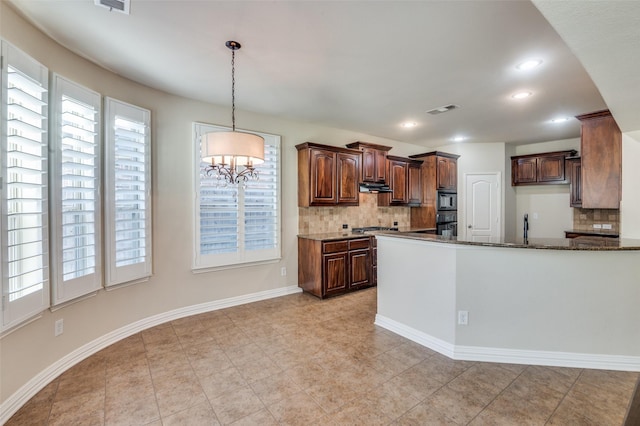 kitchen featuring pendant lighting, oven, a chandelier, decorative backsplash, and dark stone counters