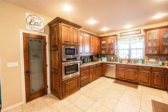 kitchen with appliances with stainless steel finishes, sink, decorative backsplash, light tile patterned floors, and light stone countertops