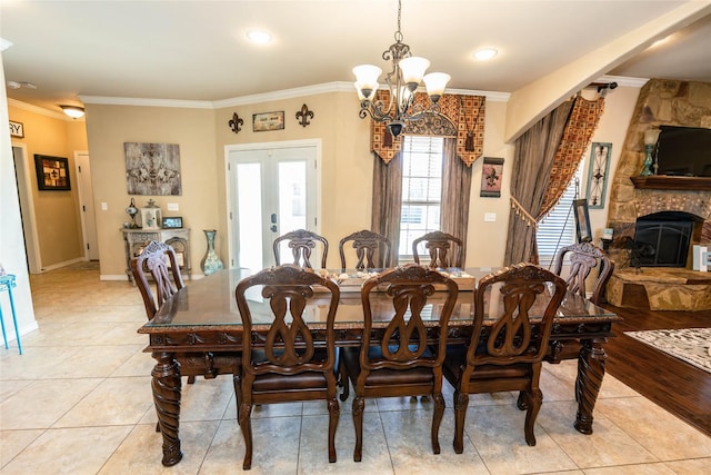 dining space featuring a fireplace, light tile patterned floors, crown molding, an inviting chandelier, and french doors