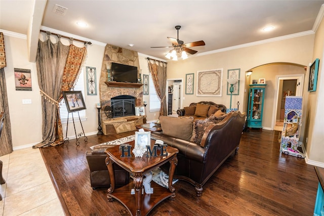 living room featuring ornamental molding, a stone fireplace, hardwood / wood-style floors, and ceiling fan