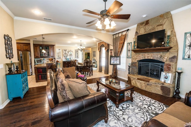 living room featuring dark wood-type flooring, a fireplace, ornamental molding, and ceiling fan with notable chandelier