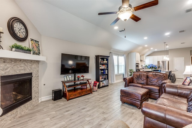 living room with a tiled fireplace, vaulted ceiling, ceiling fan, and light hardwood / wood-style flooring