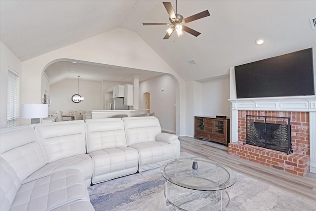 living room with ceiling fan, lofted ceiling, a fireplace, and light hardwood / wood-style flooring