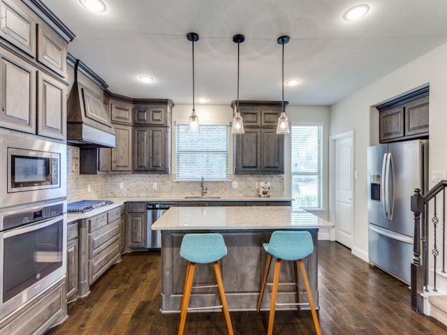 kitchen with sink, light stone counters, decorative light fixtures, a kitchen island, and stainless steel appliances