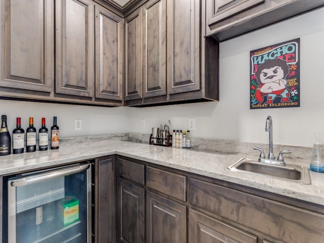 kitchen with dark brown cabinetry, beverage cooler, light stone countertops, and sink