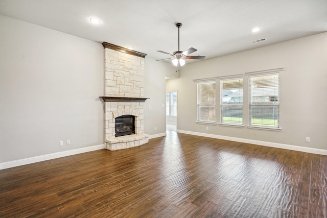 unfurnished living room featuring dark hardwood / wood-style floors, ceiling fan, and a stone fireplace