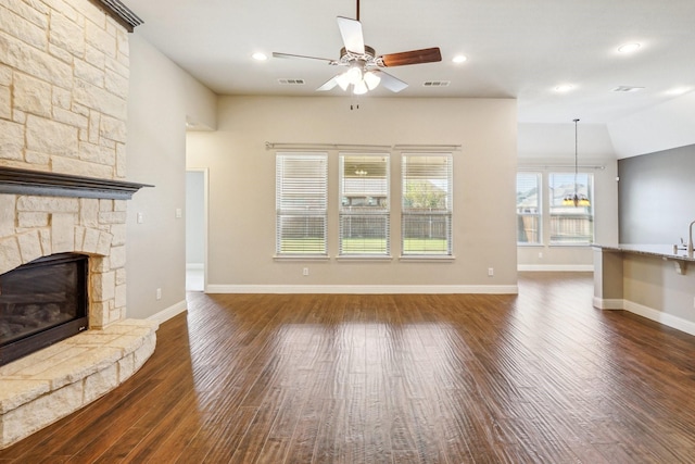 unfurnished living room featuring a stone fireplace, dark hardwood / wood-style floors, and ceiling fan