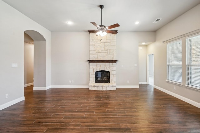 unfurnished living room featuring ceiling fan, dark hardwood / wood-style floors, and a stone fireplace