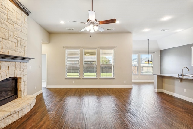 unfurnished living room featuring dark wood-type flooring, a stone fireplace, sink, vaulted ceiling, and ceiling fan