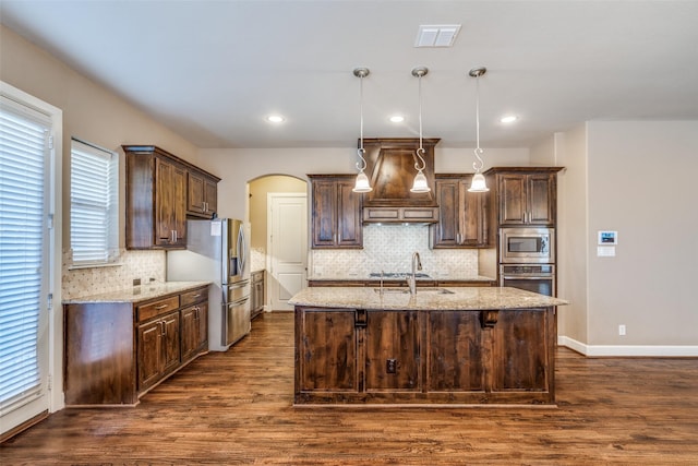 kitchen with appliances with stainless steel finishes, premium range hood, dark brown cabinetry, and arched walkways