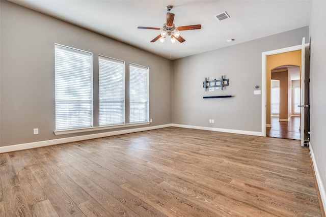 spare room with a healthy amount of sunlight, arched walkways, a ceiling fan, and light wood-style flooring