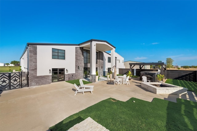 rear view of property featuring a fire pit, a hot tub, and a patio