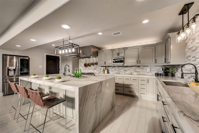 kitchen with gray cabinets, appliances with stainless steel finishes, sink, a kitchen bar, and a large island with sink