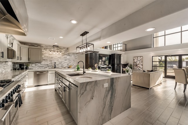 kitchen featuring appliances with stainless steel finishes, decorative light fixtures, an island with sink, sink, and light stone counters