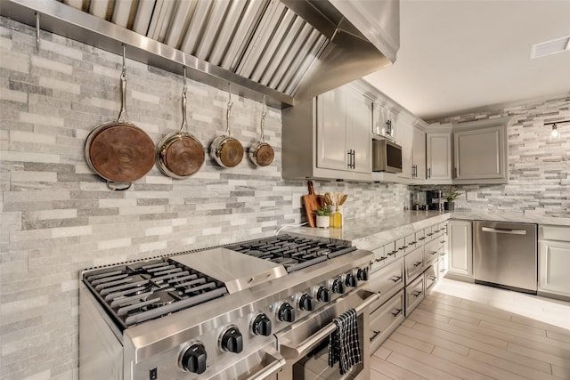 kitchen featuring light hardwood / wood-style flooring, decorative backsplash, gray cabinets, and appliances with stainless steel finishes