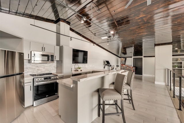 kitchen featuring appliances with stainless steel finishes, tasteful backsplash, white cabinets, a kitchen breakfast bar, and light wood-type flooring