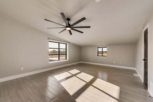 empty room featuring plenty of natural light, wood-type flooring, and vaulted ceiling