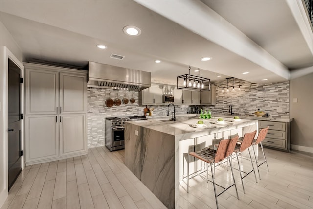 kitchen with wall chimney exhaust hood, sink, a center island with sink, gray cabinets, and stainless steel appliances