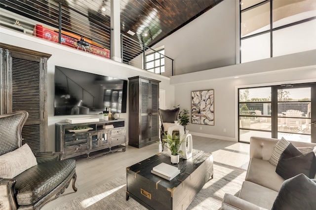 living room with a towering ceiling, a healthy amount of sunlight, and light hardwood / wood-style flooring