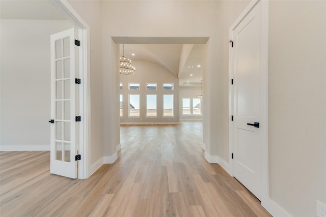 hall featuring french doors, lofted ceiling, an inviting chandelier, and light hardwood / wood-style flooring