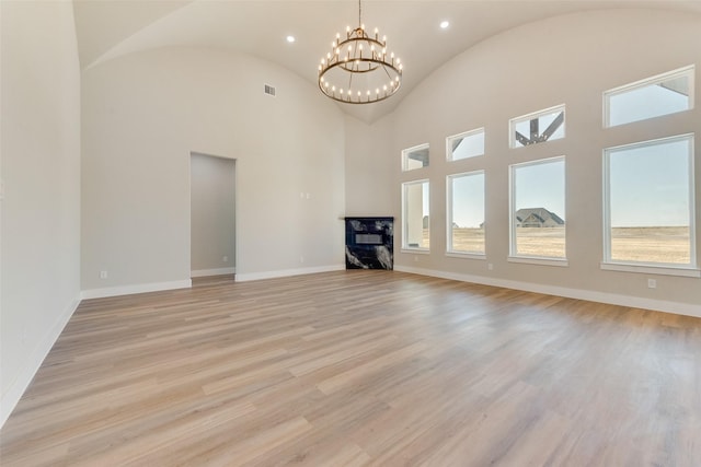 unfurnished living room featuring a premium fireplace, lofted ceiling, an inviting chandelier, and light hardwood / wood-style flooring