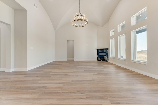 unfurnished living room with an inviting chandelier, high vaulted ceiling, and light hardwood / wood-style flooring