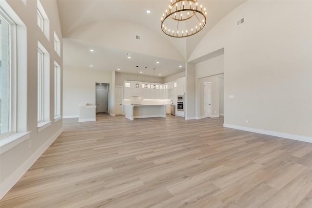 unfurnished living room with plenty of natural light, a chandelier, high vaulted ceiling, and light wood-type flooring