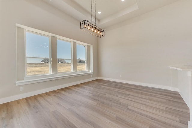 unfurnished dining area with light hardwood / wood-style flooring and a raised ceiling