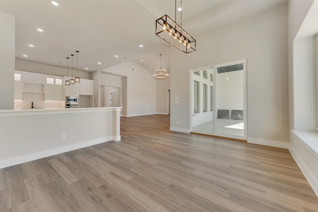 unfurnished living room with high vaulted ceiling, a chandelier, and light wood-type flooring