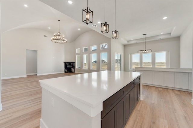 kitchen with a large island, decorative light fixtures, light hardwood / wood-style flooring, and vaulted ceiling