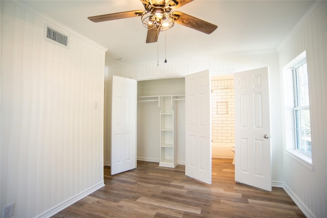 unfurnished bedroom with dark wood-type flooring, a closet, crown molding, and multiple windows