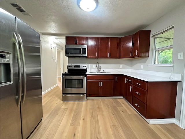 kitchen with stainless steel appliances, sink, a textured ceiling, and light wood-type flooring