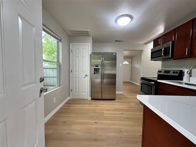 kitchen featuring stainless steel appliances, sink, light hardwood / wood-style floors, and a textured ceiling