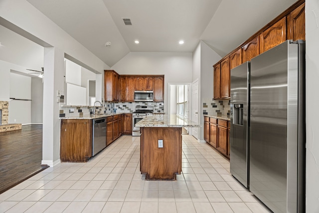 kitchen with light stone counters, light tile patterned floors, stainless steel appliances, and a center island