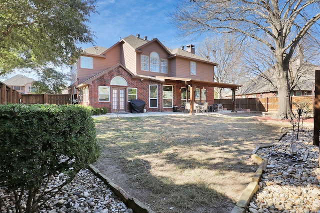 back of house with a patio, a fenced backyard, brick siding, and a chimney